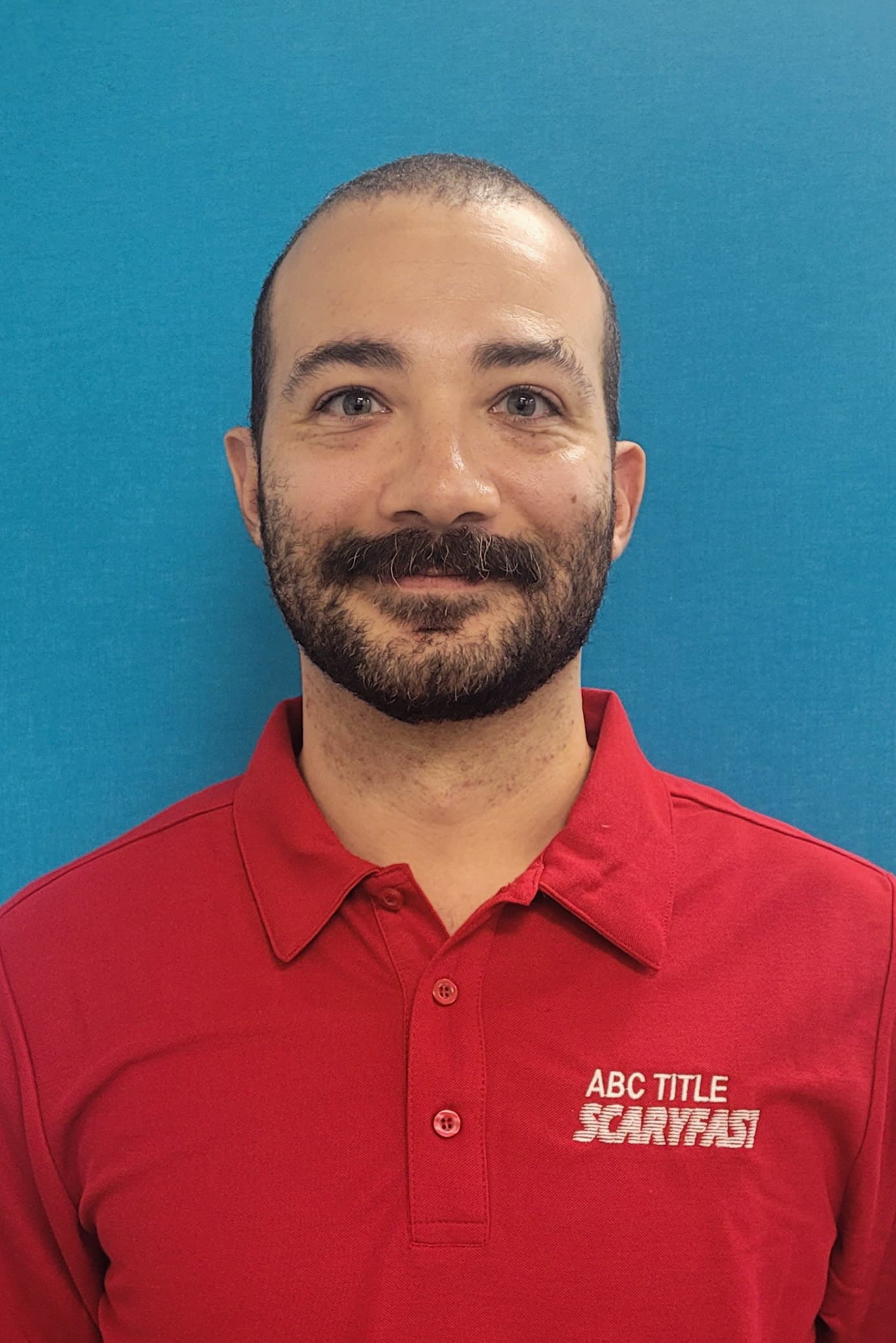 ABC Title A man with a mustache and beard, wearing a red polo shirt with the text "ABC TITLE SCARFAST," stands in front of a blue background.
